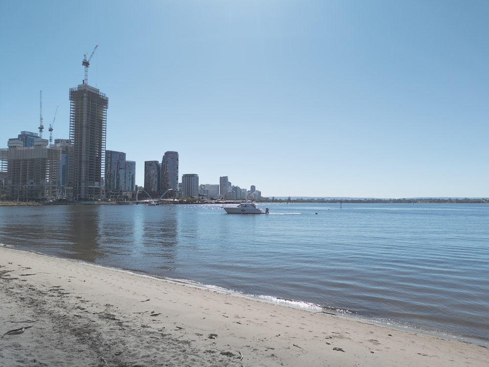 a beach with a boat in the water and a city in the background