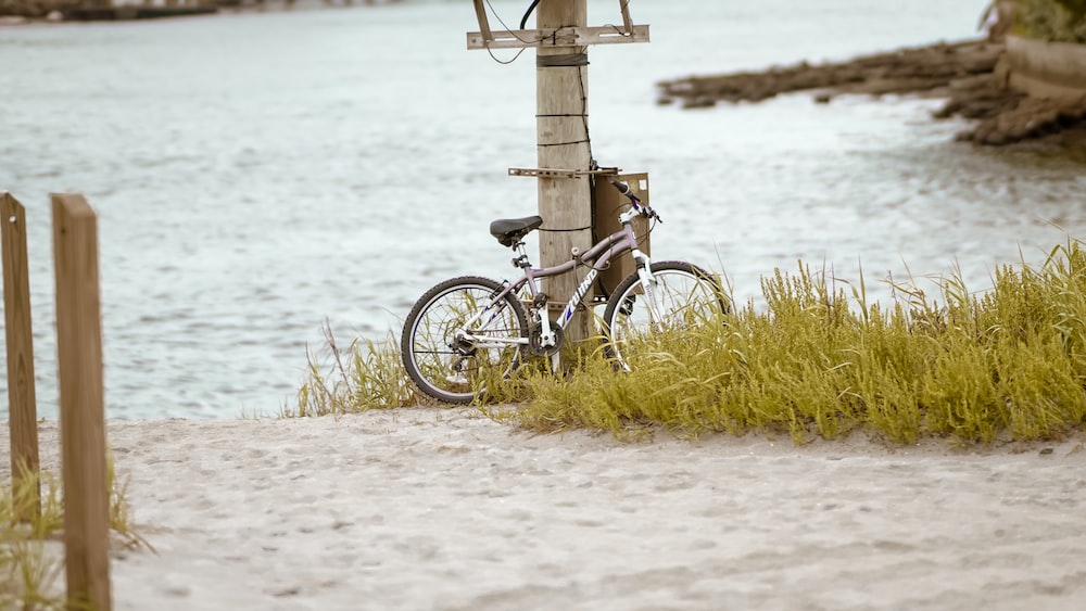 a bike parked next to a wooden post on a beach