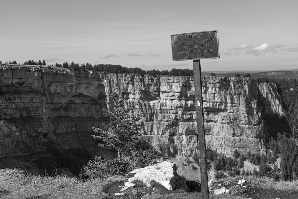 a black and white photo of a sign at the edge of a cliff