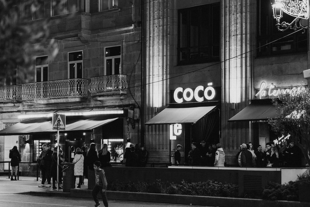 a black and white photo of people walking in front of a coco store