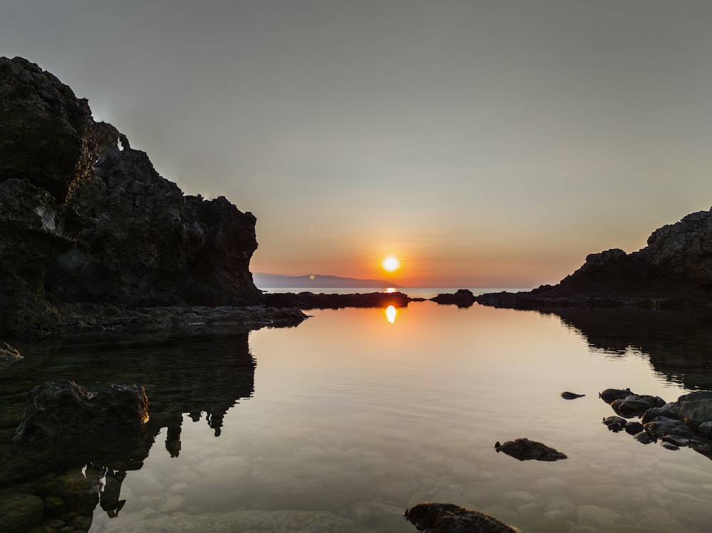 a body of water surrounded by rocks and a sunset
