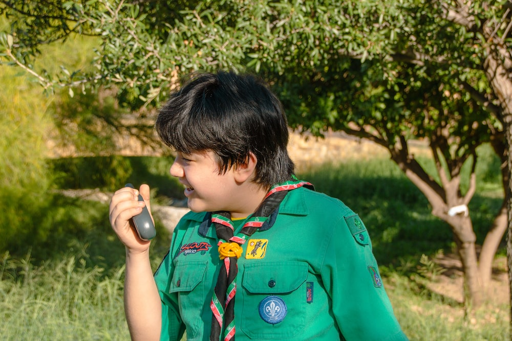 a boy in a green uniform holding a cell phone