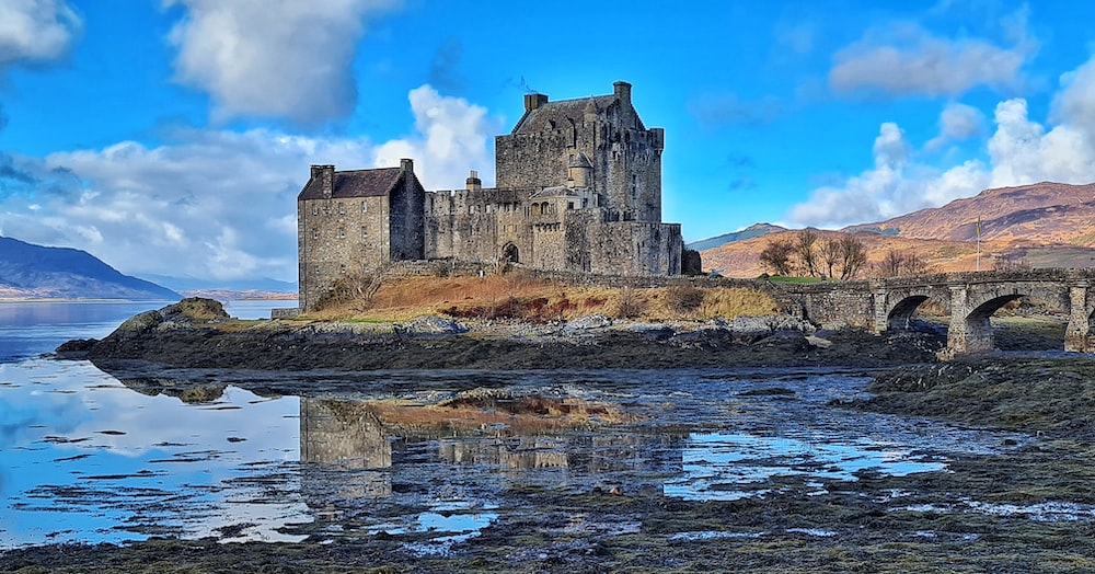 a castle on a hill by a river with Eilean Donan in the background