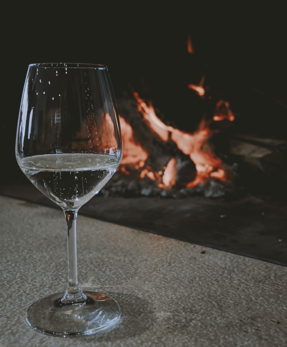 a glass of wine sitting in front of a fire