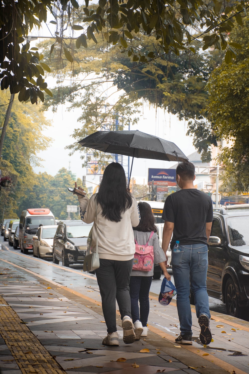 a group of people walk down a sidewalk under an umbrella