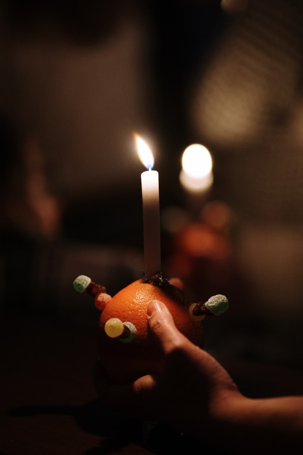 a hand holding an orange with a candle in it