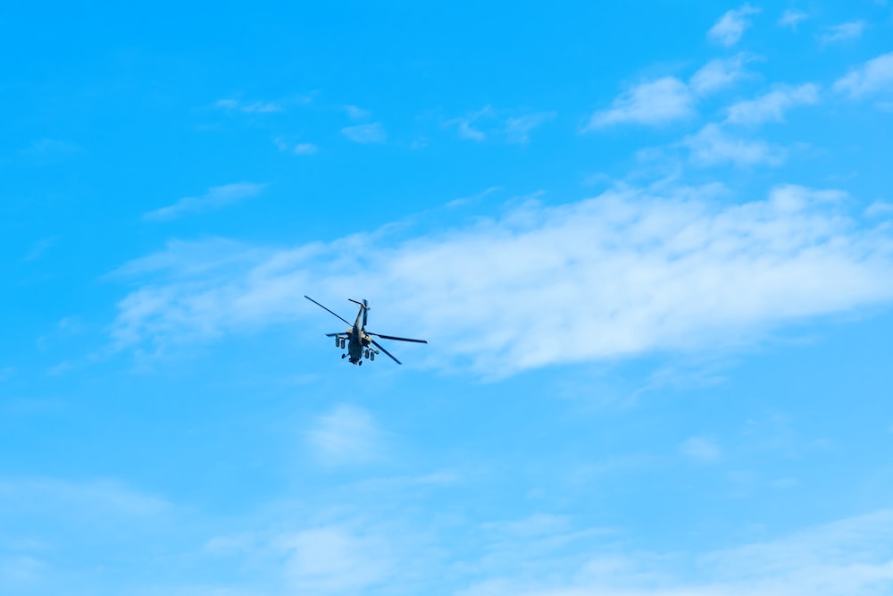 a helicopter flying through a blue cloudy sky