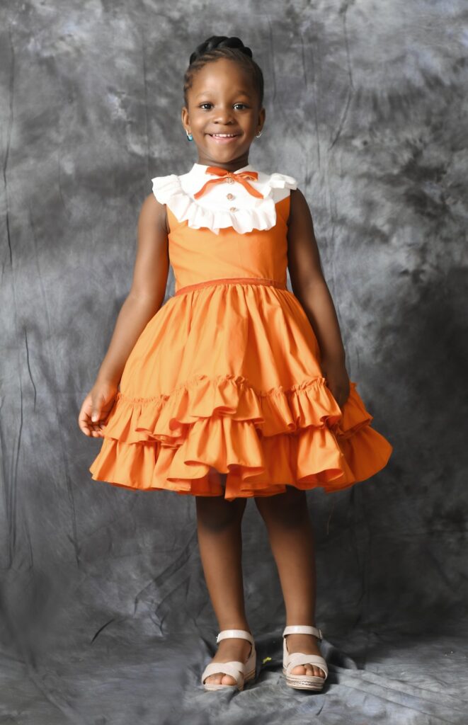 a little girl in an orange dress posing for a picture