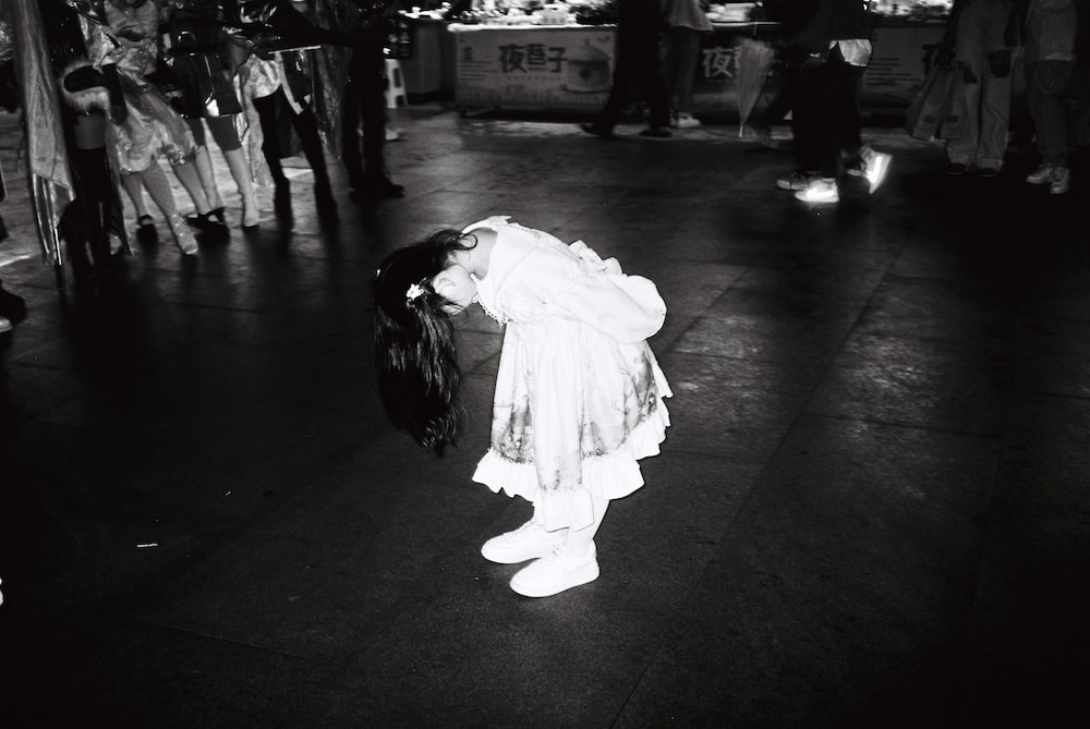 a little girl in a white dress standing on a sidewalk