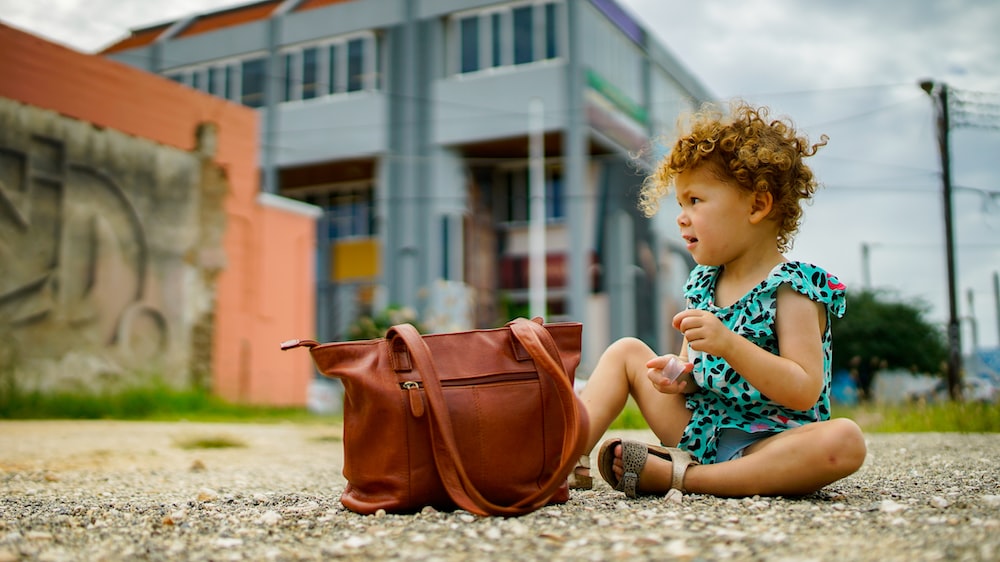 a little girl sitting on the ground next to a purse