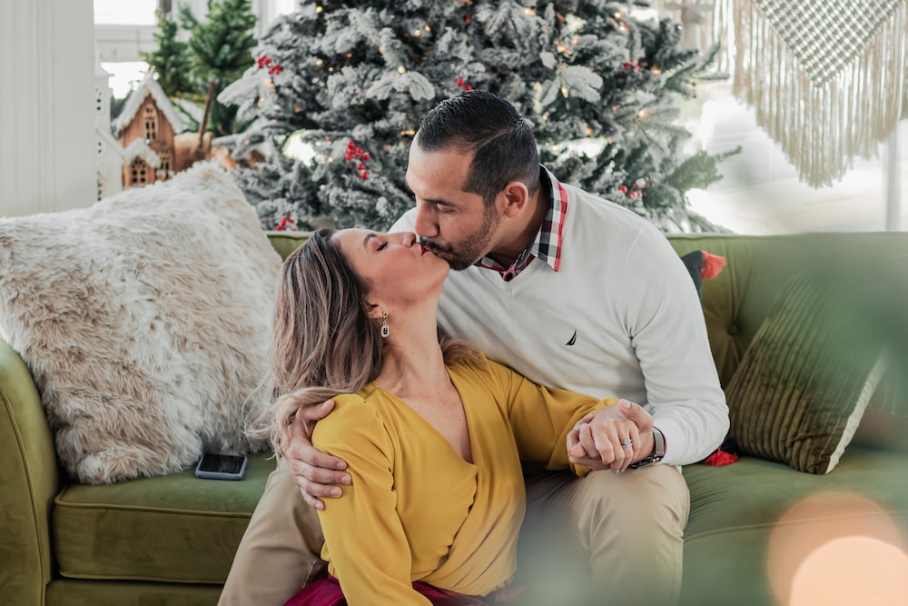 a man and woman kissing on a couch in front of a christmas tree