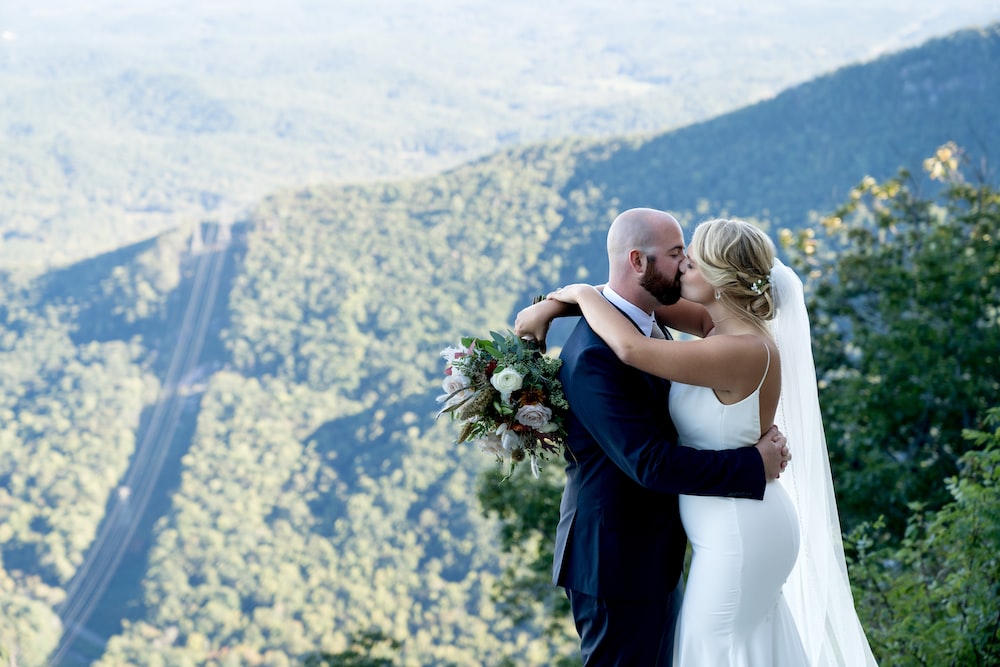 a man and woman kissing on a hilltop overlooking a valley