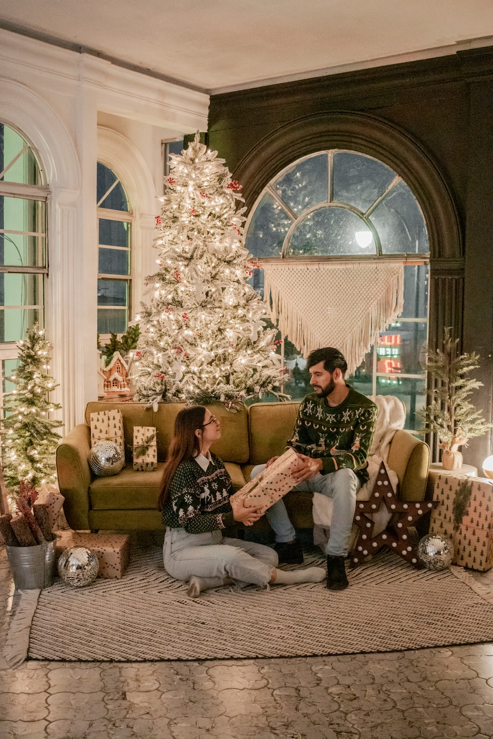 a man and woman sitting on a couch in front of a decorated tree