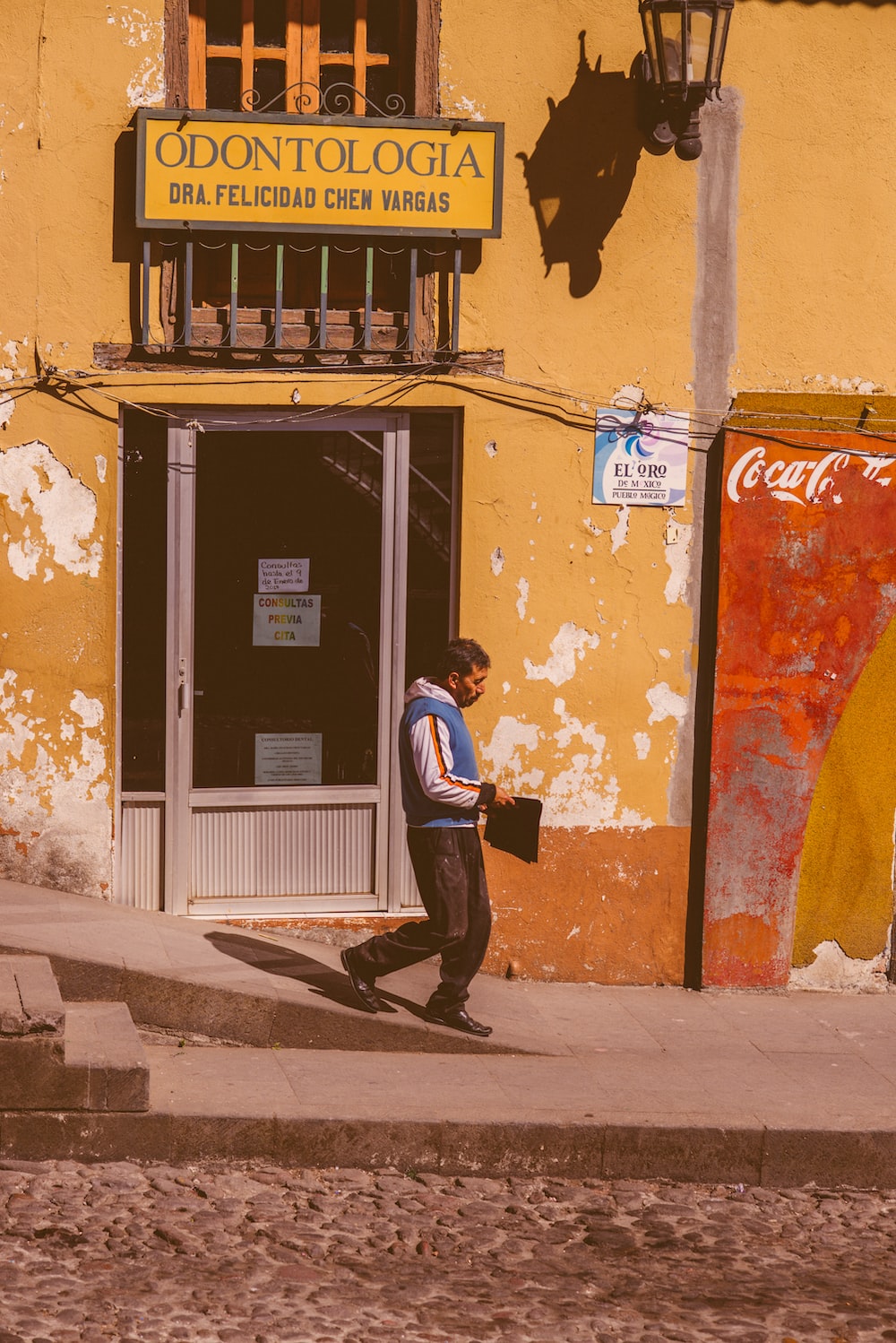 a man walking down a street past a yellow building