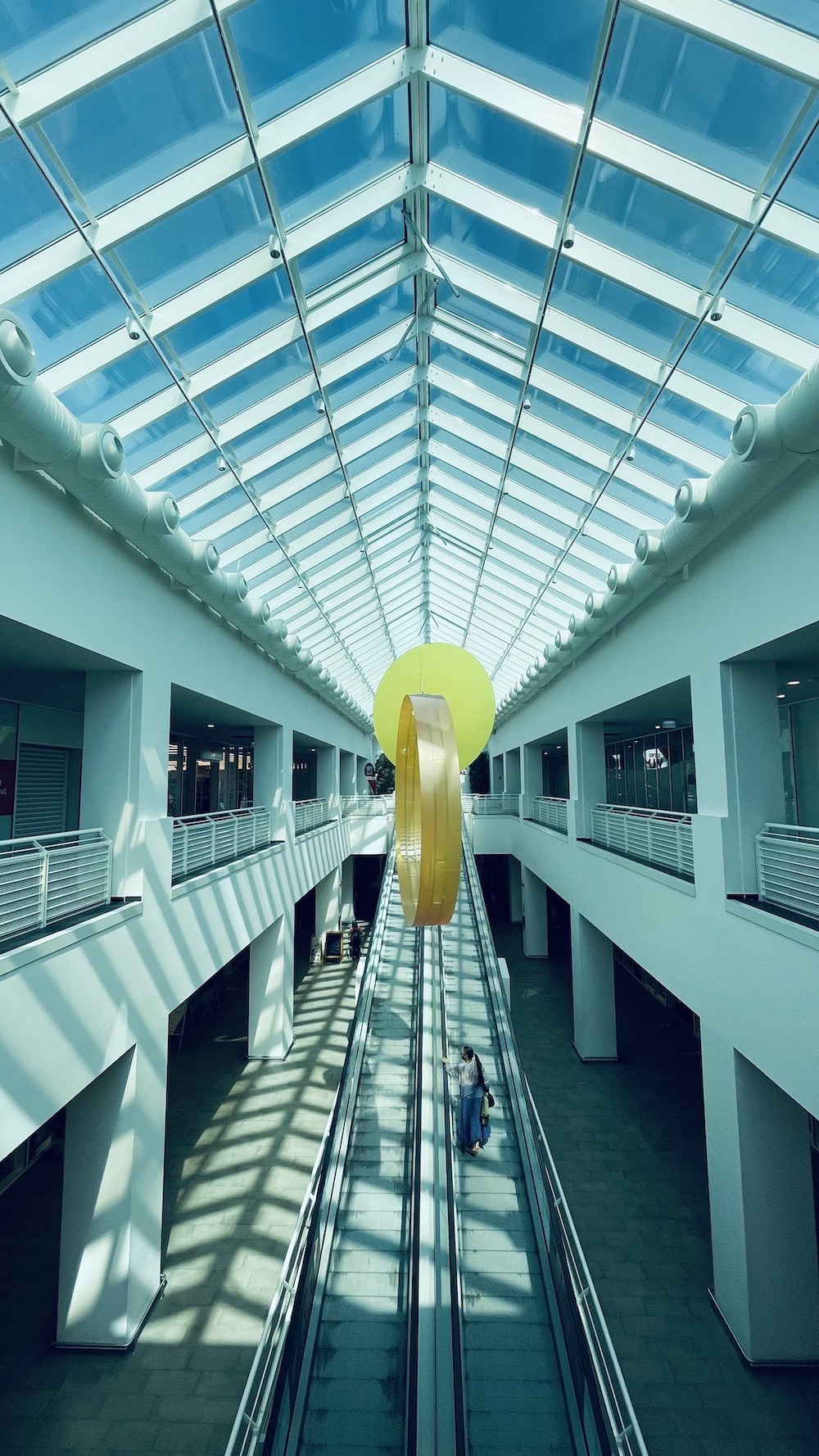 an escalator in a building with a large yellow object hanging from the ceiling