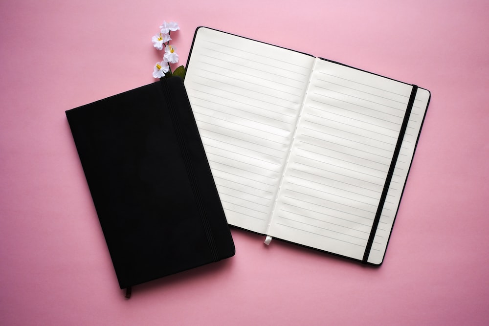 a notebook with a pen and flower on a pink background