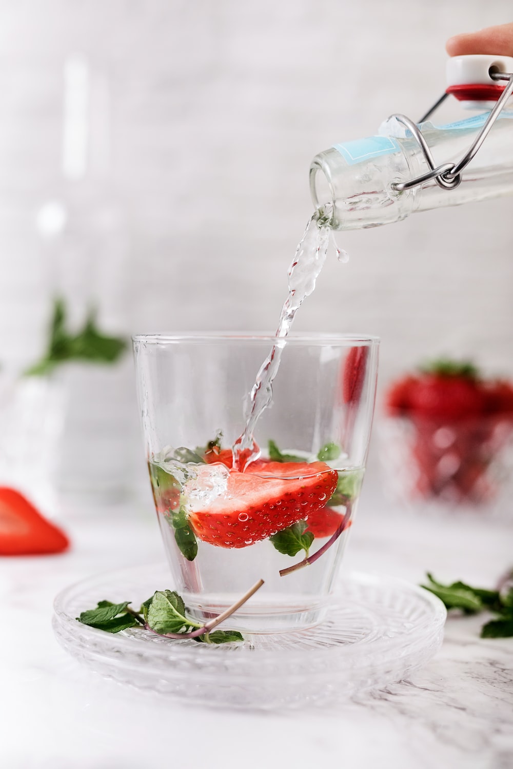 a person pouring water into a glass filled with strawberries