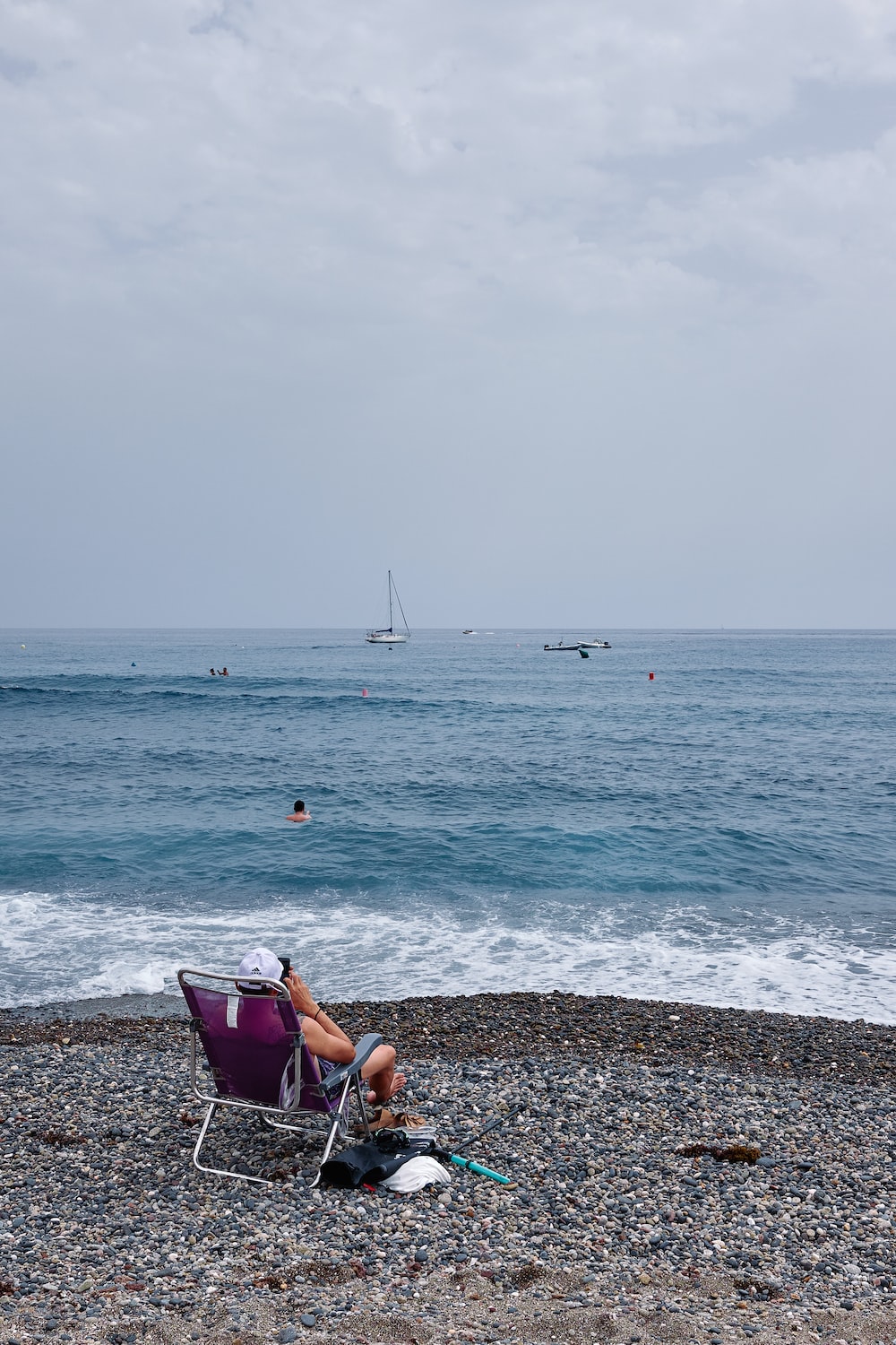 a person sitting in a chair on a beach looking at a sailboat