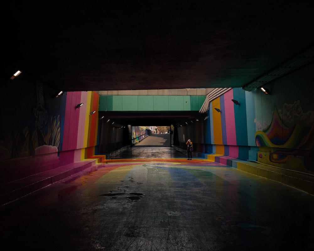 a person standing in a tunnel with a rainbow painted wall