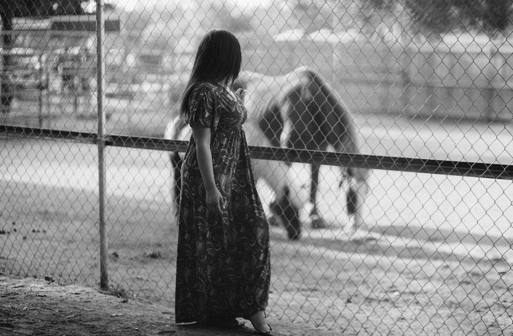 a person standing in front of a fence looking at a dog