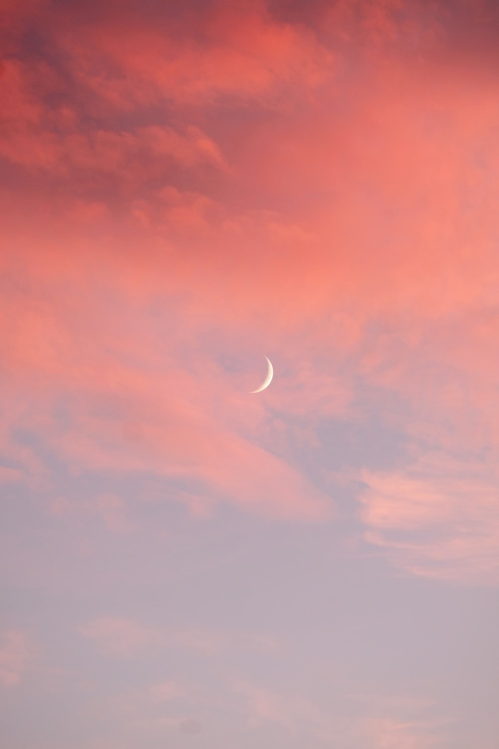 a pink and blue sky with a crescent moon in the middle