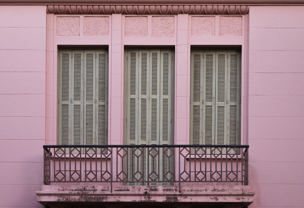 a pink building with two windows and a balcony