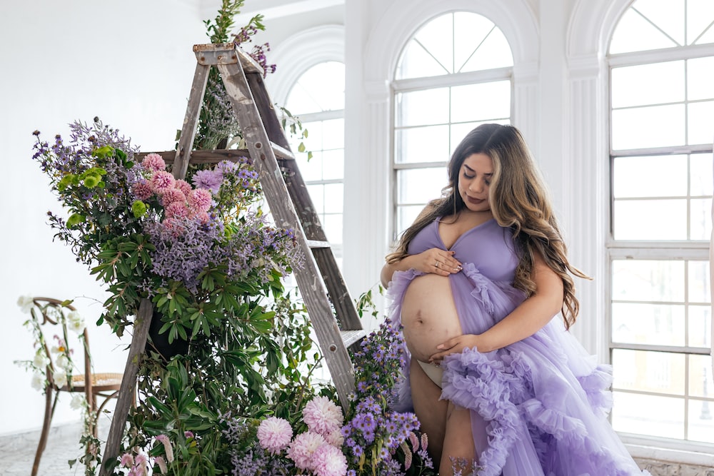 a pregnant woman in a purple dress standing next to a ladder