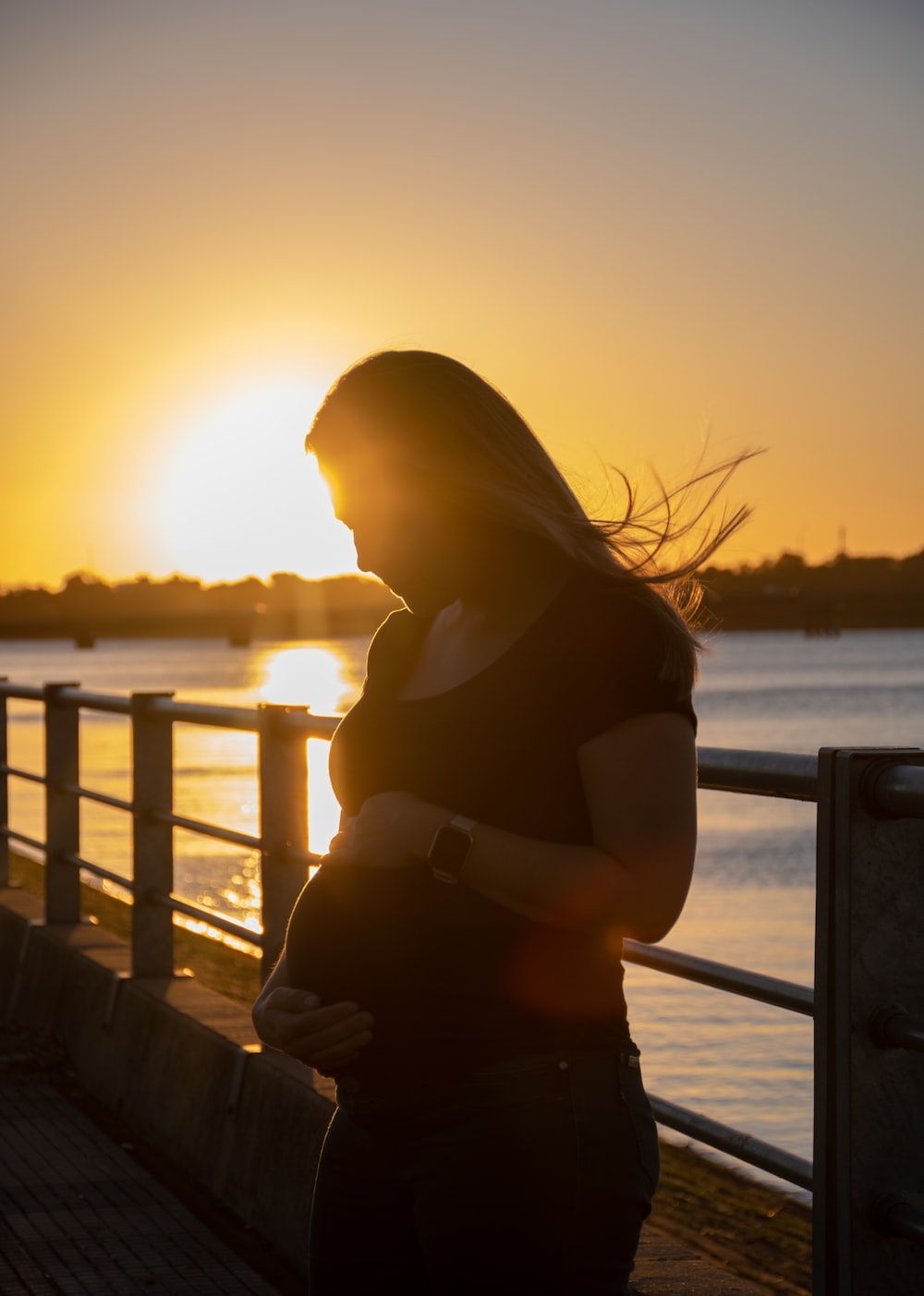 a pregnant woman standing next to a body of water