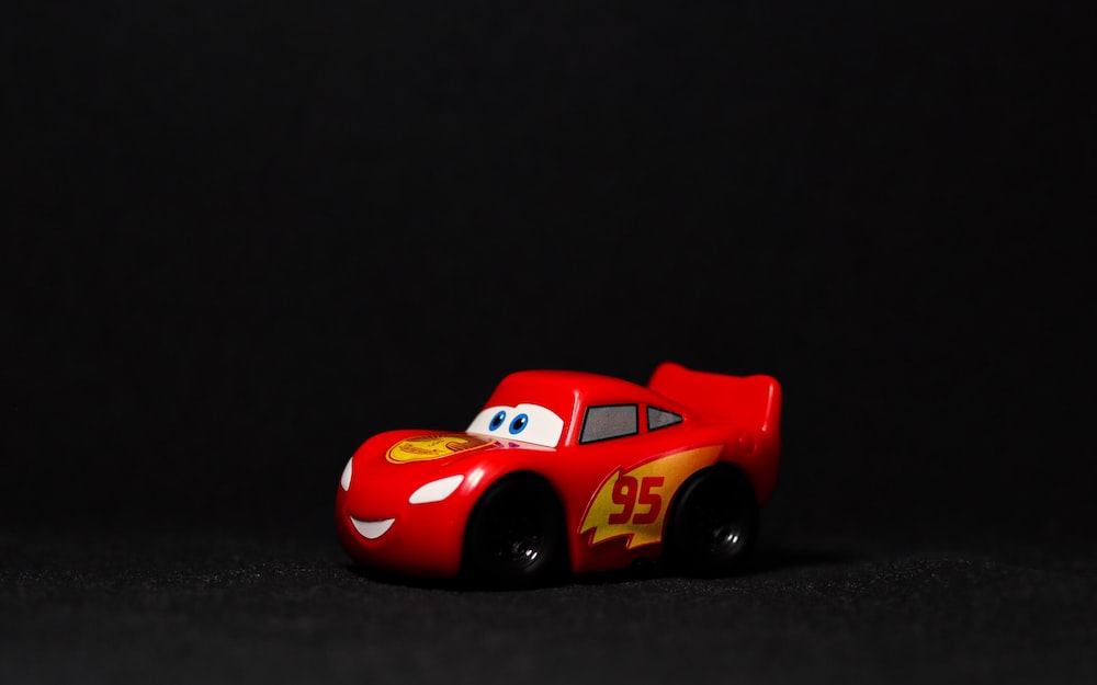 a red toy car sitting on top of a black surface