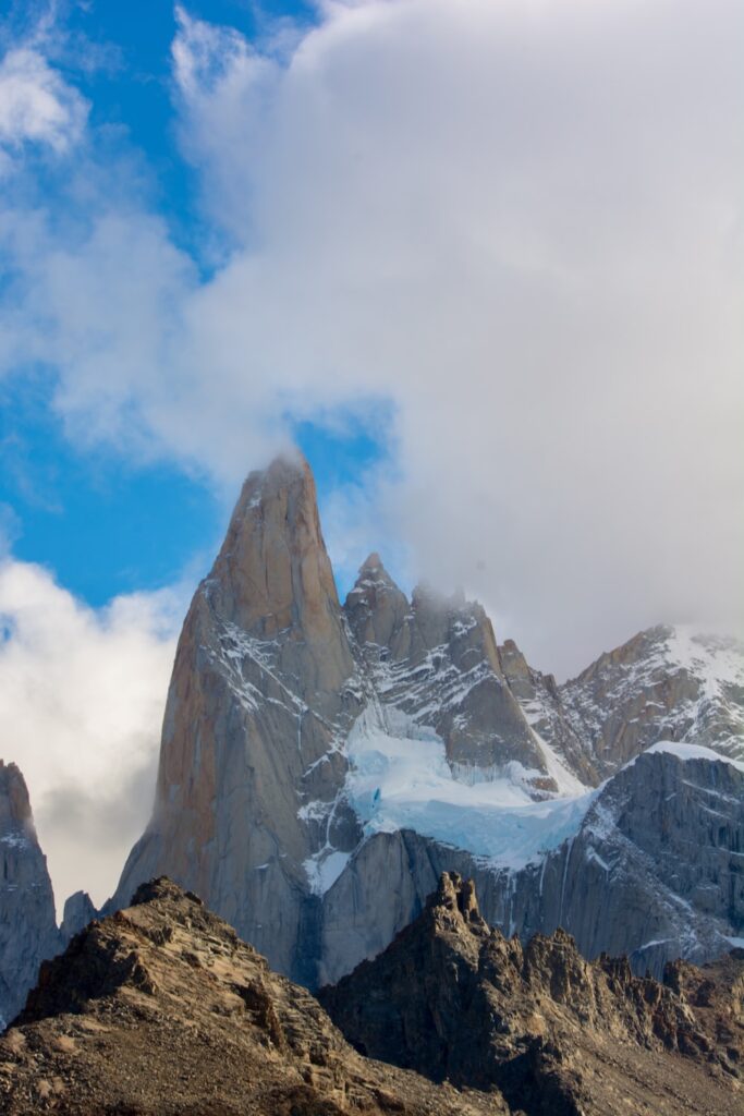 a snowy mountain with clouds with Fitz Roy in the background