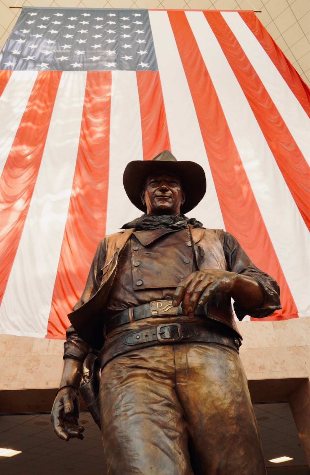 a statue of a man in a cowboy hat with an american flag in the background