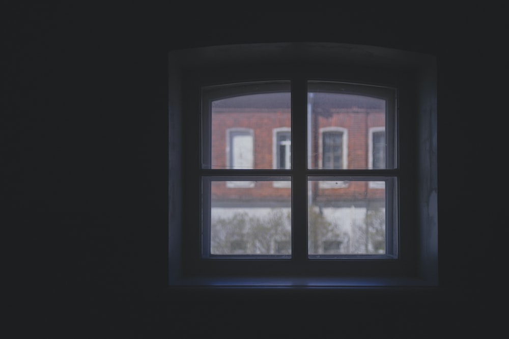 a window in a dark room with a brick building in the background