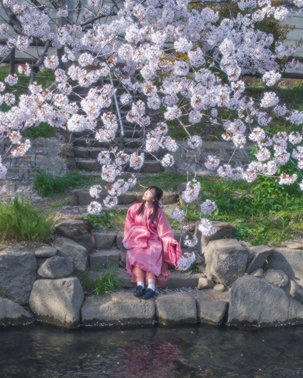 a woman in a pink kimono sitting on rocks next to a pond