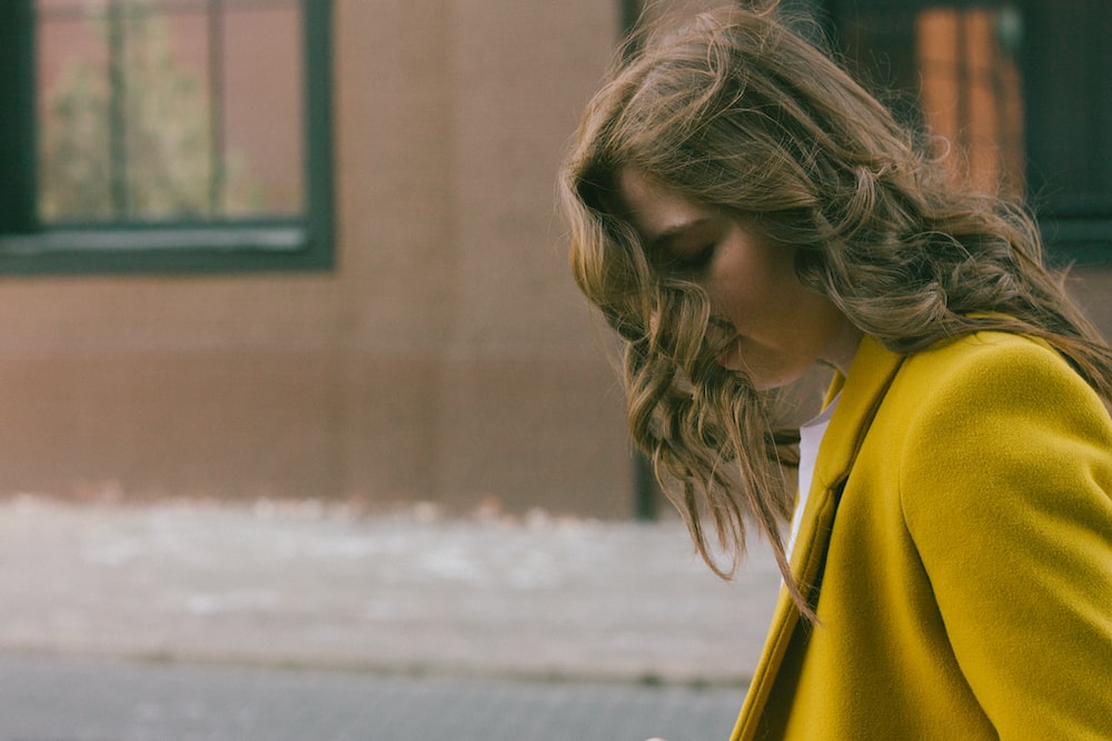 a woman in a yellow coat is looking at her cell phone