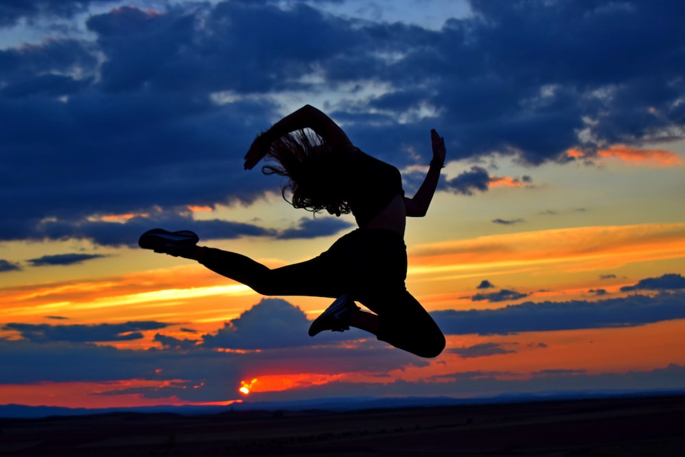 a woman jumping in the air at sunset