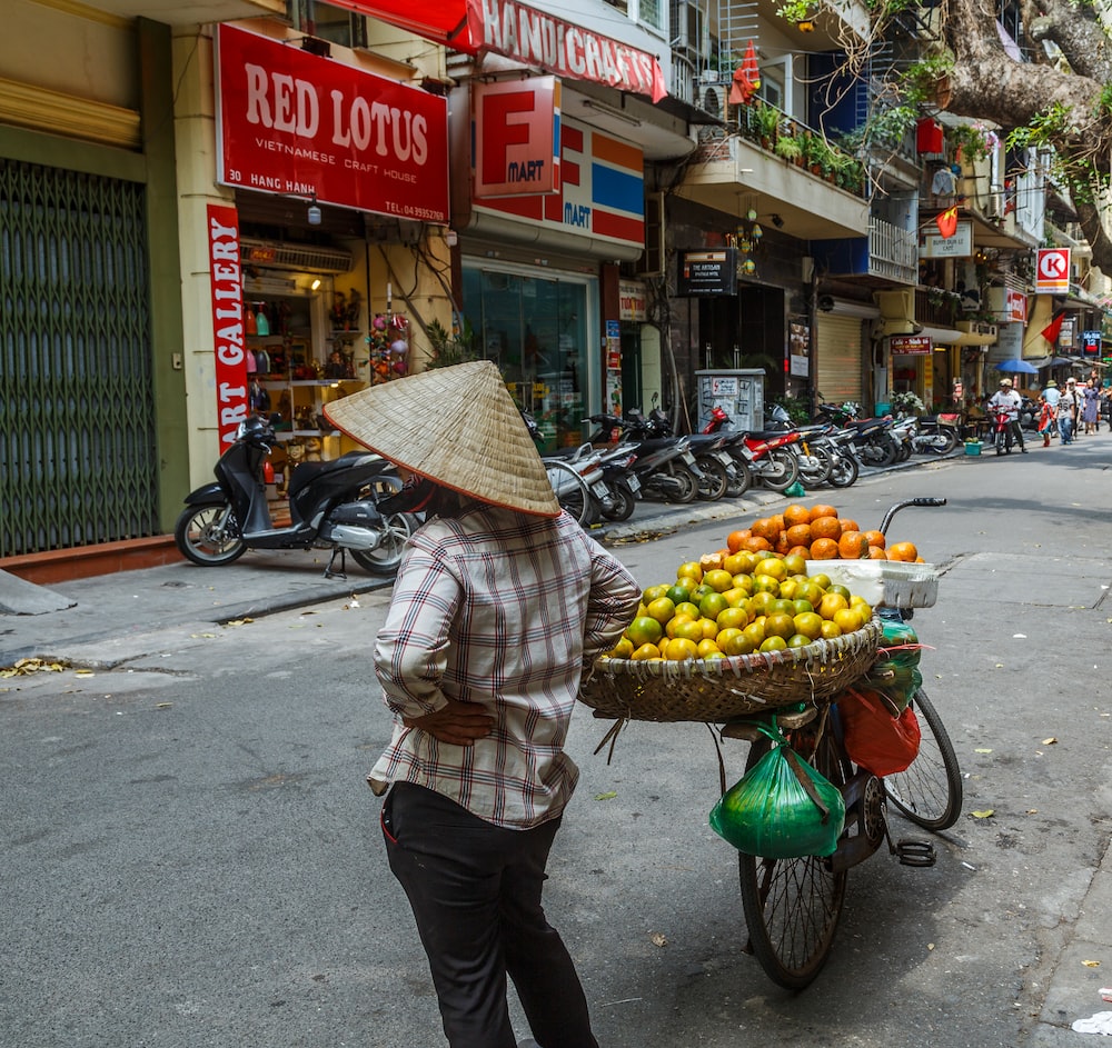 a woman pushing a cart full of fruit down a street