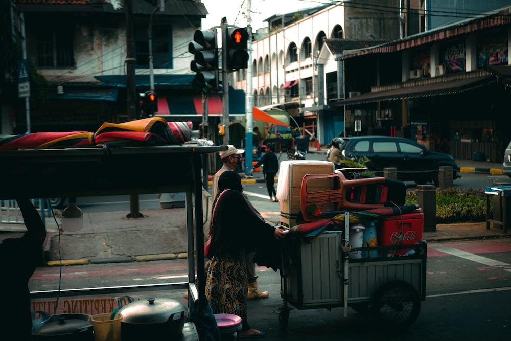 a woman pushing a cart with luggage on it down a street