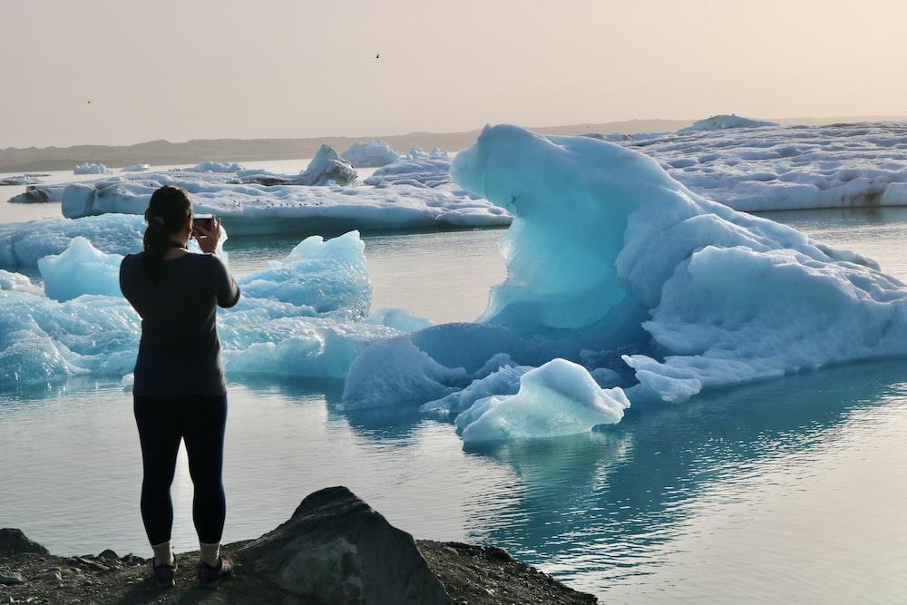 a woman taking a picture of icebergs in the water