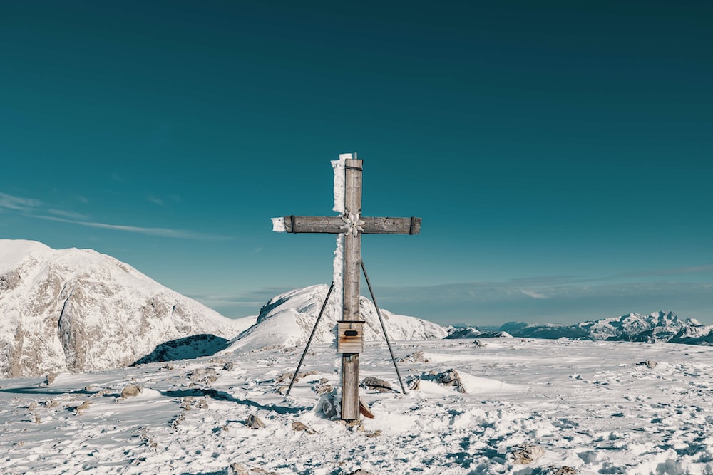 a wooden cross on top of a snow covered mountain