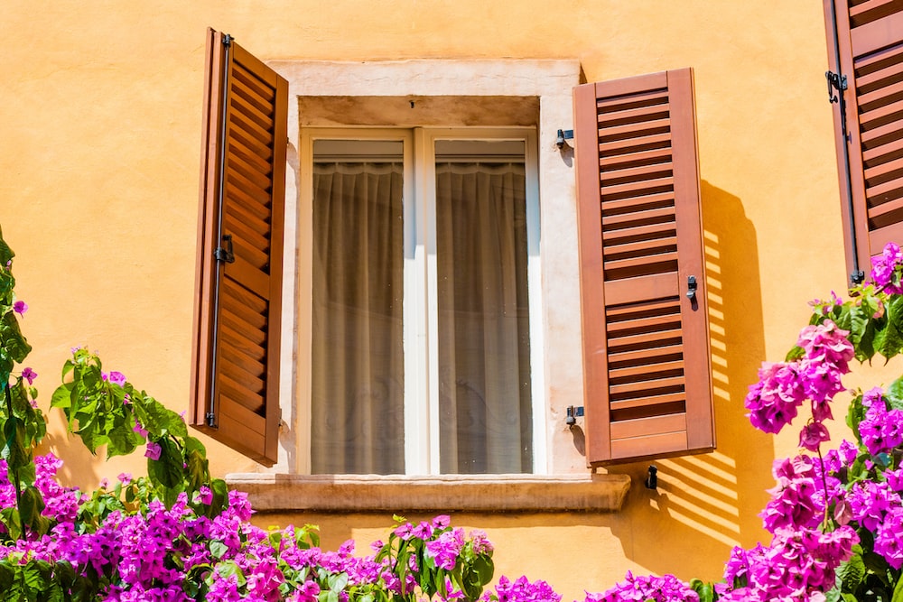 a yellow building with red shutters and purple flowers
