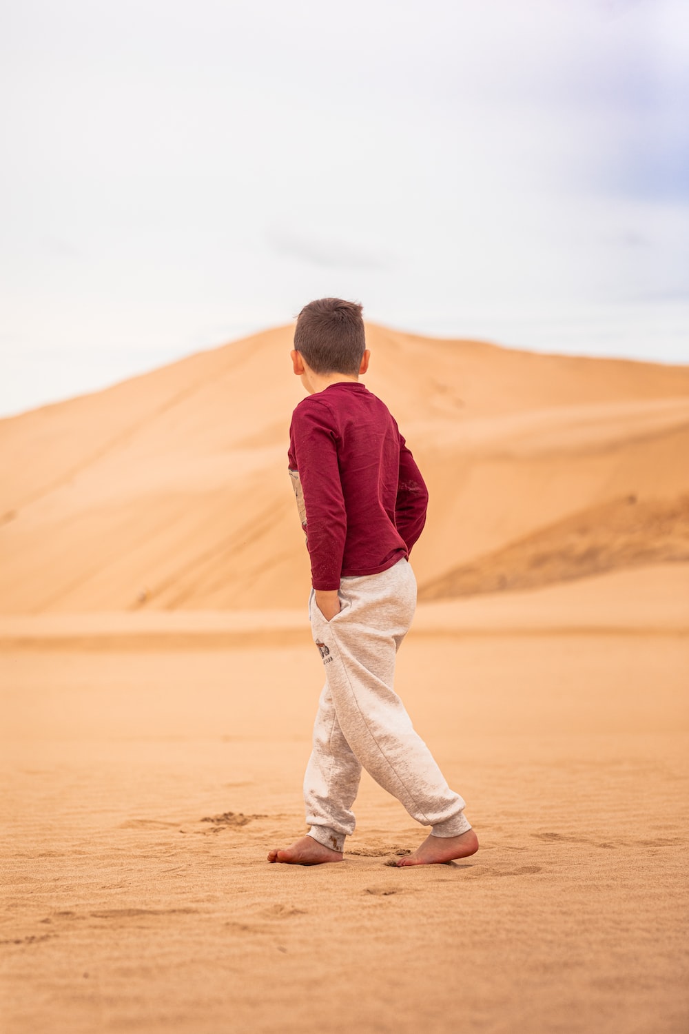 a young boy walking across a sandy field