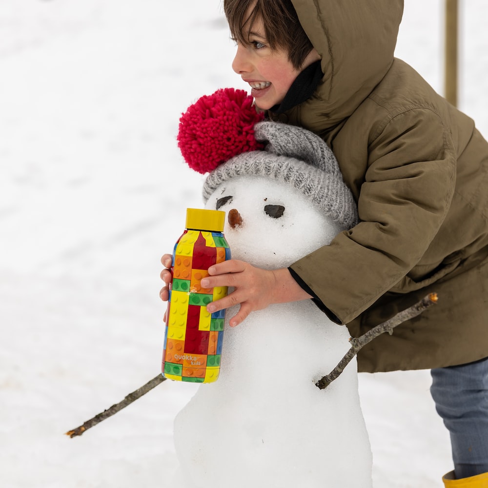 girl in brown jacket holding white snowman