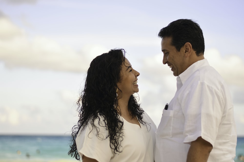 man and woman facing each other while smiling at the beach