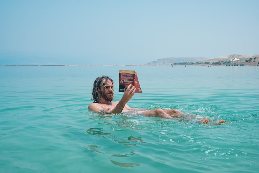 man floating on body of water while reading book