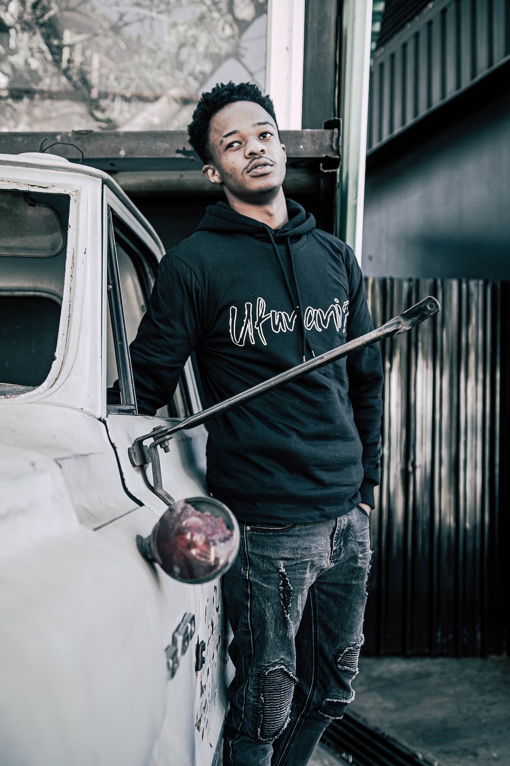 man in black and white pullover hoodie and blue denim jeans standing beside white car