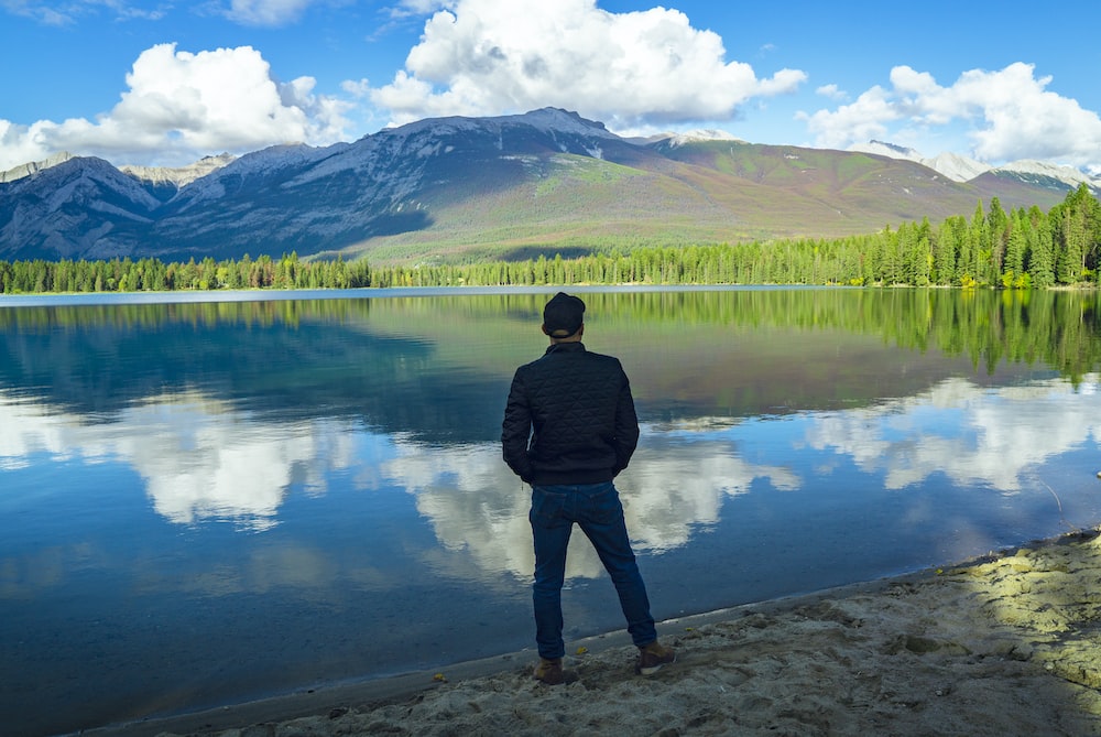 man in black jacket standing near lake during daytime