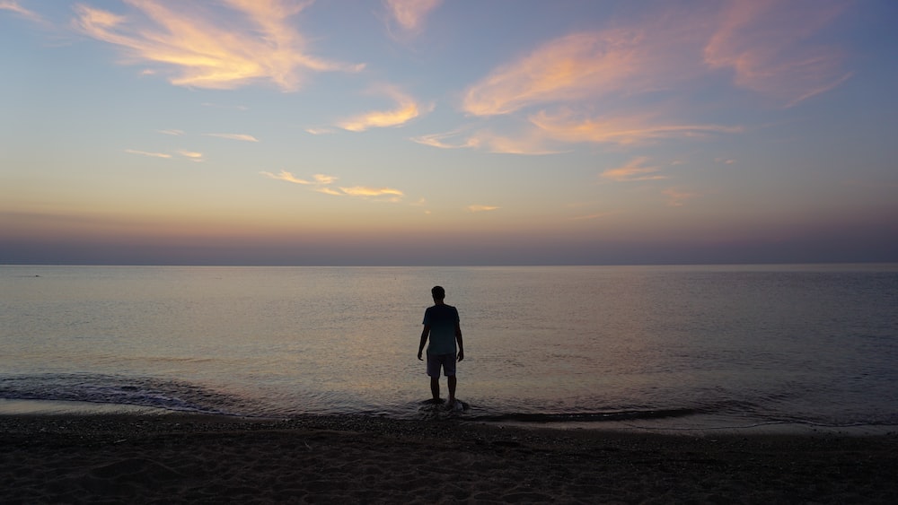 man in black jacket standing on seashore during sunset