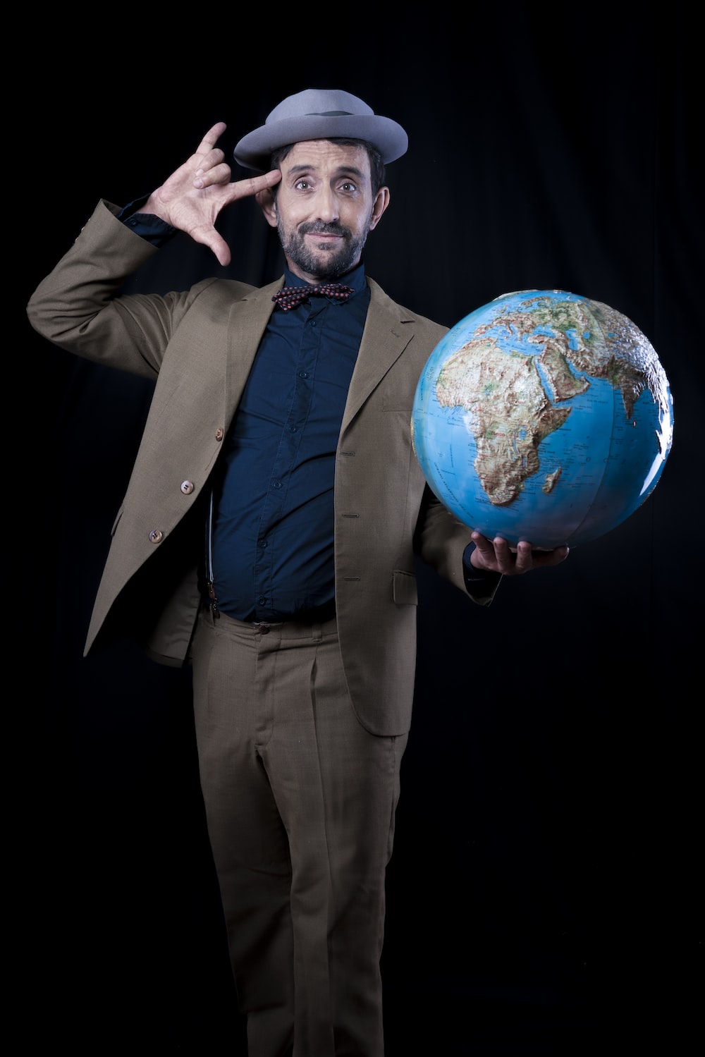 man in brown suit jacket and dress pants holding planet earth toy