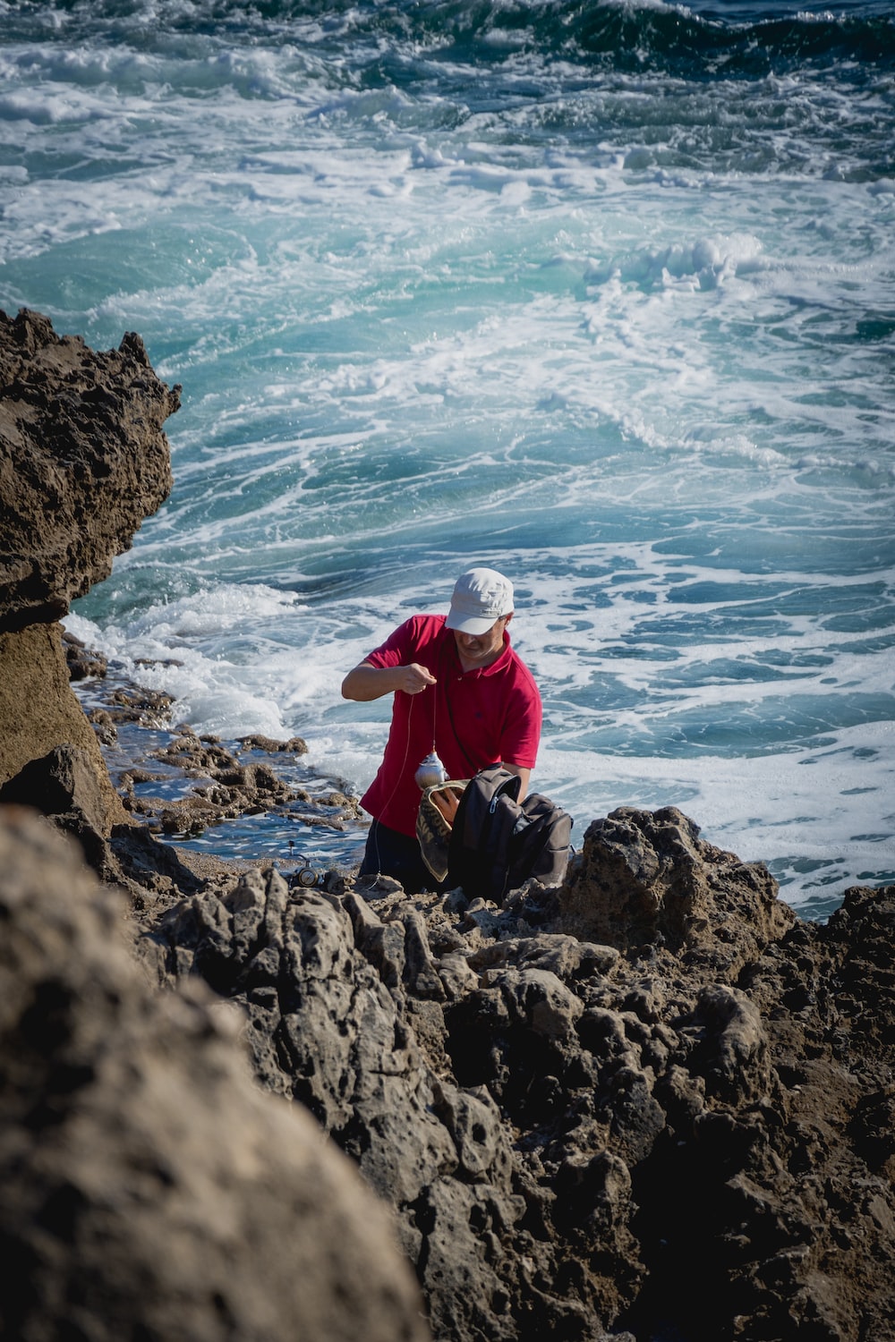 man in red jacket sitting on rock formation near sea during daytime