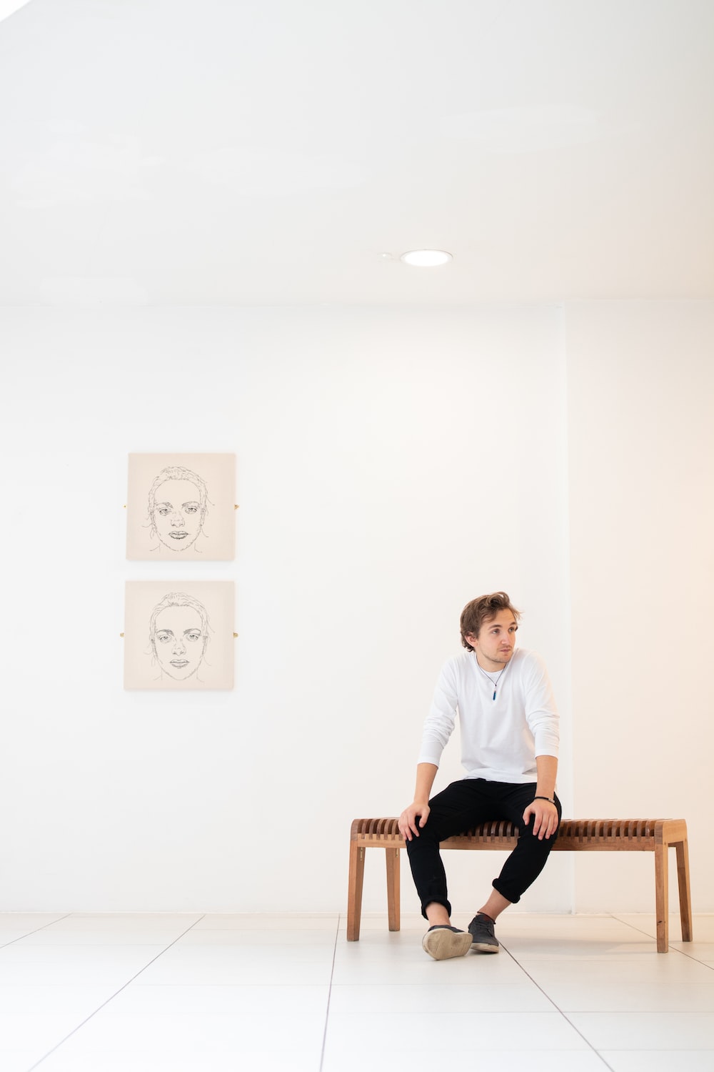 man in white shirt sitting on bench beside portraits